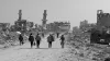 Displaced Palestinians walk down a road between bombed-out buildings in Gaza
