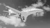 A white private jet flies against a partly cloudy sky, seen from below