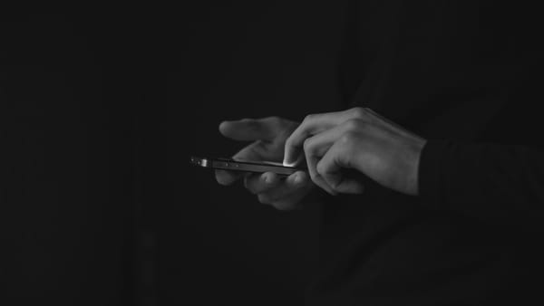 A pair of hands using a smartphone emerge from the darkness