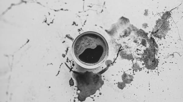 A cup of black coffee on a stained and cracked table surrounded by spilled coffee